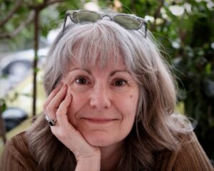 A smiling gray-haired woman wearing sunglasses on her head smiles straight at the camera.